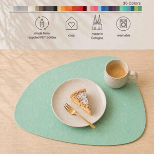 May include: A light green felt placemat with a plate, fork, and mug on top. The plate holds a slice of cake. The mug contains a beverage. The placemat is made from recycled PET bottles and is washable.