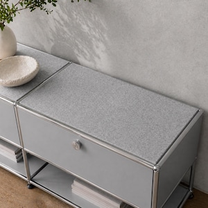 Könnte beinhalten: Ein moderner, modularer grauer Schrank mit einer gesprenkelten grauen Oberseite und Chromleisten. Der Schrank hat Schubladen mit runden silbernen Knöpfen und offenen Regalen. Eine weiße Schale und eine Vase mit Grünzeug stehen oben.