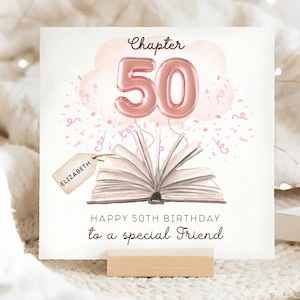 May include: A birthday card with a watercolor illustration. The card features an open book with the number 50 in pink balloon letters, a pink cloud, and confetti. The text reads "Chapter 50" and "Happy 50th Birthday to a special Friend". A tag with the name "Elizabeth" is attached.