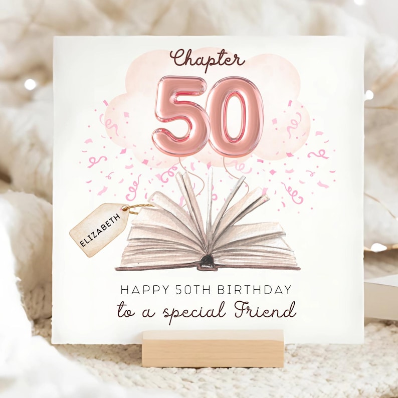 May include: A birthday card with a watercolor illustration. The card features an open book with the number 50 in pink balloon letters, a pink cloud, and confetti. The text reads "Chapter 50" and "Happy 50th Birthday to a special Friend". A tag with the name "Elizabeth" is attached.