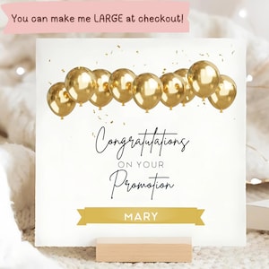 Puede incluir: Tarjeta de felicitación blanca con globos dorados y la frase "Congratulations on Your Promotion". Una pancarta dorada en la parte inferior dice "MARY". La tarjeta se muestra en un soporte de madera.