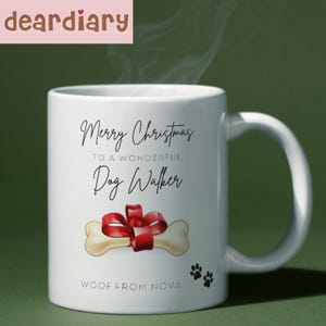 May include: White ceramic mug with the text "Merry Christmas to a Wonderful Dog Walker." Features a bone with a red bow and paw prints. The mug also has the text "Woof from Nova."