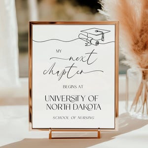 May include: A gold-framed sign with the text "My next chapter begins at University of North Dakota School of Nursing". The sign features a line drawing of a graduation cap and diploma.