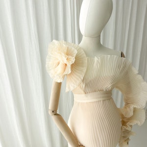 Detail shot of the dramatic ruffle sleeve in Creamy Peach. The pleated fabric holds its sculptural shape, making it a powerful statement piece for outdoor photography during the golden hour.