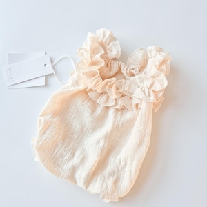 Romantic newborn photo props. Vanilla off-white baby romper featuring an oversized, highly textured ruffle collar. Soft, breathable cotton fabric designed for elegant studio portraits and zero-friction outfit changes.