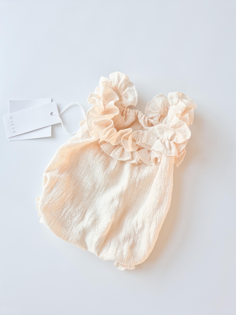Romantic newborn photo props. Vanilla off-white baby romper featuring an oversized, highly textured ruffle collar. Soft, breathable cotton fabric designed for elegant studio portraits and zero-friction outfit changes.