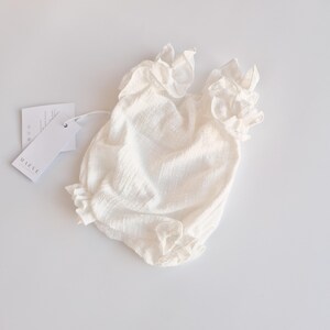 Angled view of an ivory newborn romper highlighting the comfortable smocked bodice and elasticized leg openings. The breathable cotton design ensures a zero-friction fit, essential for a cozy hello world outfit.