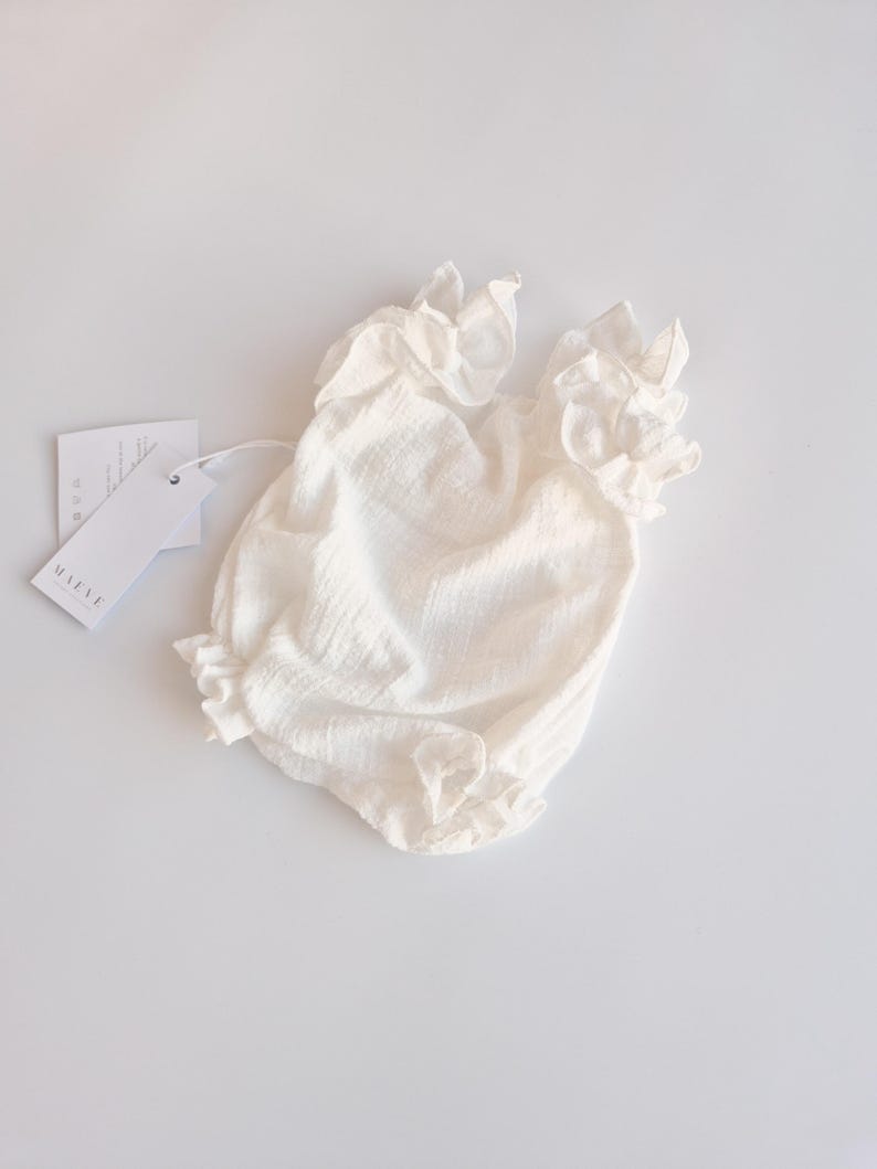Angled view of an ivory newborn romper highlighting the comfortable smocked bodice and elasticized leg openings. The breathable cotton design ensures a zero-friction fit, essential for a cozy hello world outfit.