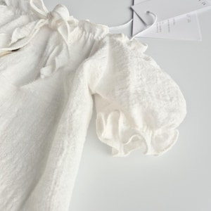Detailed macro shot of an ivory infant outfit highlighting the dainty puff sleeve and soft woven texture. A perfect zero-prep newborn photo prop, capturing romantic simplicity and earthy elegance for professional lifestyle galleries.