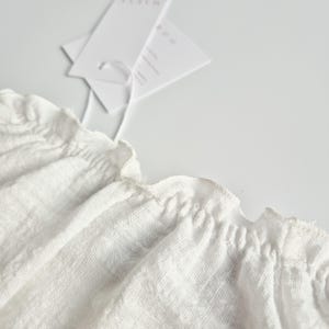 Extreme close-up of the 2-in-1 elastic neckline on a white crinkle cotton baby romper. The flexible, smocked design ensures quick outfit changes, making it a highly functional baby hospital outfit that prioritizes newborn comfort.