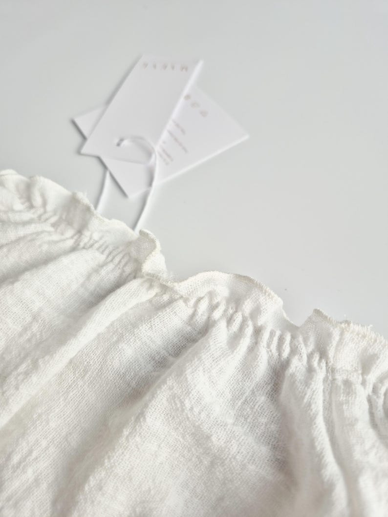 Extreme close-up of the 2-in-1 elastic neckline on a white crinkle cotton baby romper. The flexible, smocked design ensures quick outfit changes, making it a highly functional baby hospital outfit that prioritizes newborn comfort.
