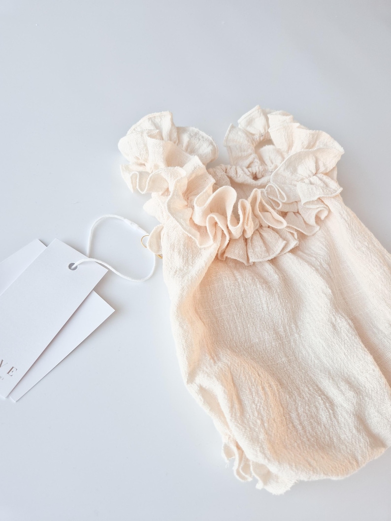 High-stretch newborn romper in creamy vanilla hue. Premium textured cotton fabric with intricate frilled shoulder details. Timeless newborn girl clothes perfect for natural light photography and cohesive maternal styling.