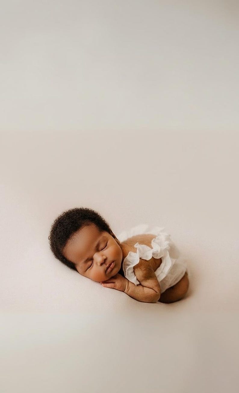 Sleeping infant wearing an ivory off-white newborn outfit, posed on a soft neutral backdrop. Close-up highlights the 3D hand-pleated back ruffles. A classic minimalist baby romper perfect for timeless, low-friction photography.