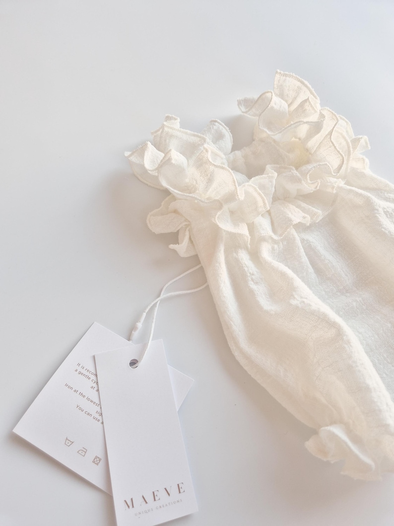 Close-up of smocked baby clothes detailing a hand-pleated ruffle neckline. The breathable ivory cotton weave shows deep textural shadows, highlighting the premium fabric quality perfect for a baptism gift girl.