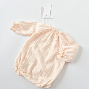 Flat lay of the Lylou warm vanilla long-sleeve baby romper with brand tags attached. A curated newborn gift showcasing buttery soft crinkled cotton and timeless minimalist baby girl clothes design.