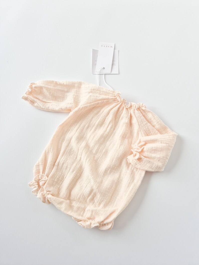 Flat lay of the Lylou warm vanilla long-sleeve baby romper with brand tags attached. A curated newborn gift showcasing buttery soft crinkled cotton and timeless minimalist baby girl clothes design.