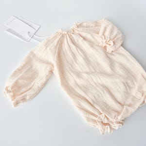 Front view flat lay of the Lylou infant romper highlighting the breathable crinkled cotton weave and keyhole button detail. A versatile, neutral-toned newborn outfit perfect for vintage studio styling.