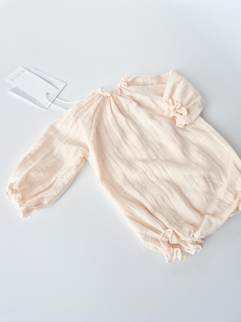 Front view flat lay of the Lylou infant romper highlighting the breathable crinkled cotton weave and keyhole button detail. A versatile, neutral-toned newborn outfit perfect for vintage studio styling.