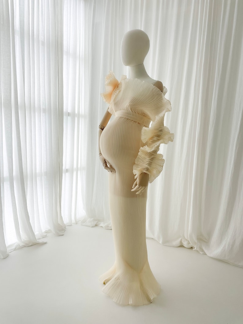 Close-up view of the fitted torso of the Celessia gown. The apricot pleated fabric hugs the bump and flows into a mermaid silhouette, highlighting the rich texture of the light-catching material.