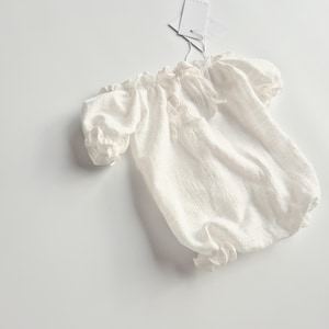 vory newborn romper displayed on a crisp white studio surface. Featuring breathable, pure crinkle cotton and delicate ruffled leg holes, these smocked baby clothes offer a high-end, zero-prep tactile foundation for photographers.