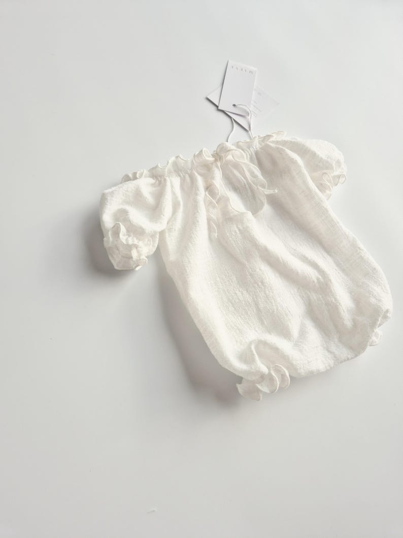 vory newborn romper displayed on a crisp white studio surface. Featuring breathable, pure crinkle cotton and delicate ruffled leg holes, these smocked baby clothes offer a high-end, zero-prep tactile foundation for photographers.