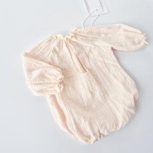 Angled flat lay shot emphasizing the nostalgic, earthy vibe of the Lylou baby romper in warm vanilla. A cherished newborn keepsake bridging functional daily wear with high-end photography styling.