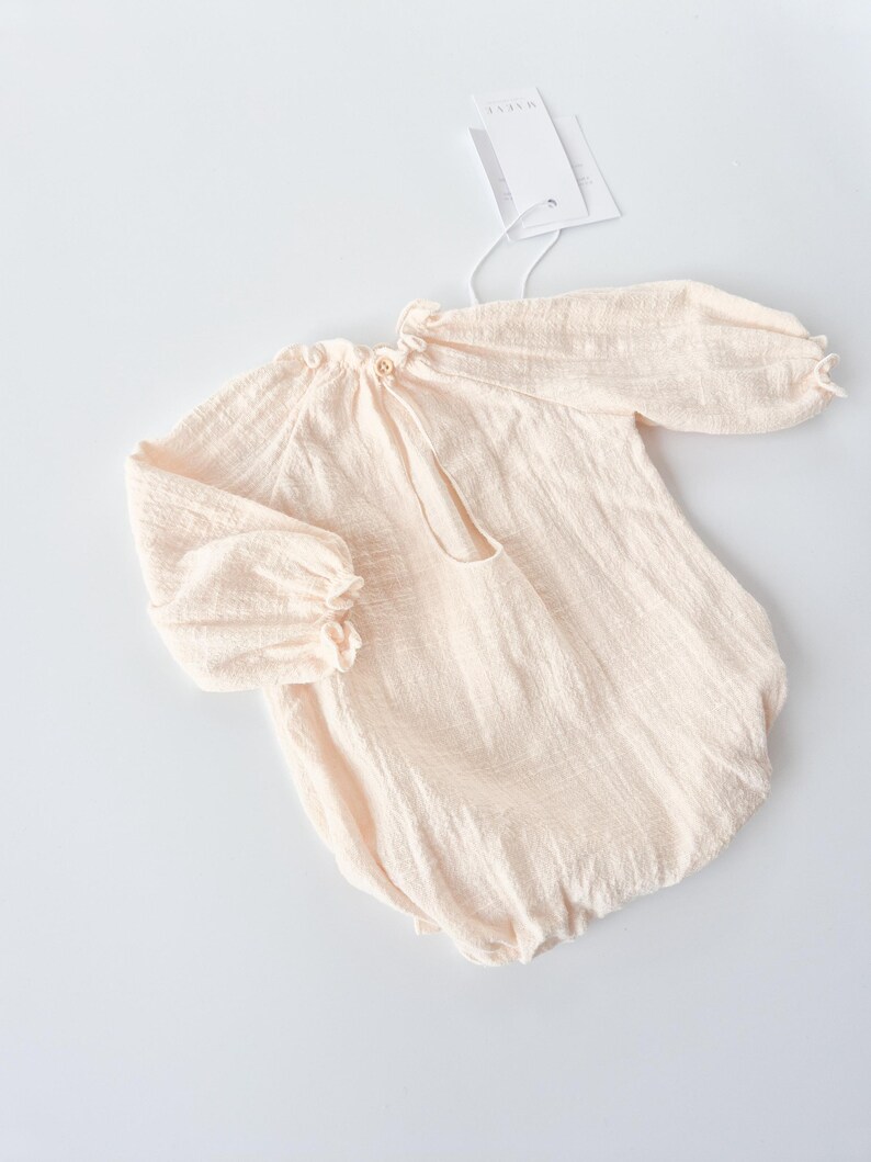 Angled flat lay shot emphasizing the nostalgic, earthy vibe of the Lylou baby romper in warm vanilla. A cherished newborn keepsake bridging functional daily wear with high-end photography styling.