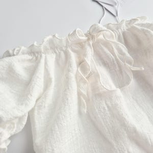 Detailed view of an elegant tie-back closure on a pure white textured baby outfit. The soft crinkle cotton and delicate bow add a touch of vintage charm, creating a heartwarming coming home outfit and versatile newborn photo prop.