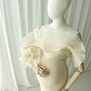 Mannequin detail shot showcasing the voluminous, sculptural ruffle sleeve of the Celessia gown. The warm peach color of the finely pleated fabric is ideal for complementary golden hour outdoor photography.