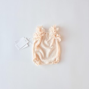 Elegant off-white newborn gift set flat lay on a bright background. Vanilla cotton baby romper with a delicate, romantic frame. Cherished newborn keepsake capturing pure innocence without the harshness of stark white fabrics.