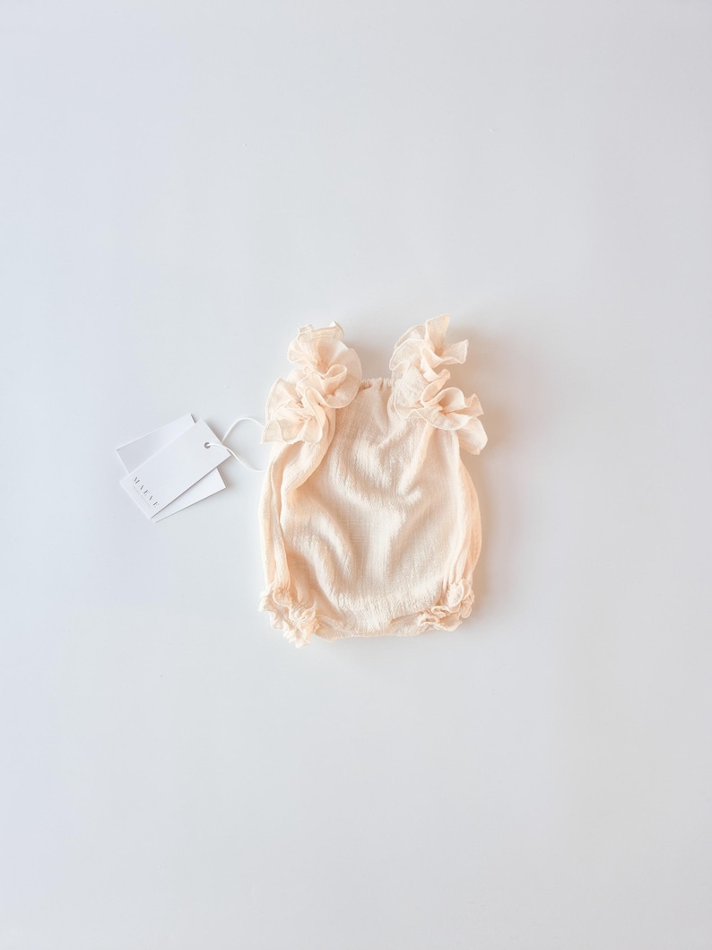 Elegant off-white newborn gift set flat lay on a bright background. Vanilla cotton baby romper with a delicate, romantic frame. Cherished newborn keepsake capturing pure innocence without the harshness of stark white fabrics.