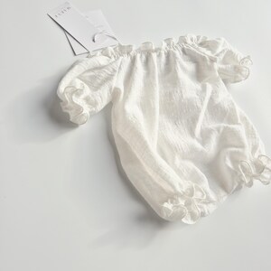 Angled studio shot of an ivory infant romper emphasizing the organic, highly textured crinkle cotton weave. This effortless, no-iron photography prop provides a luminous and tactile visual element for professional flat lay setups.