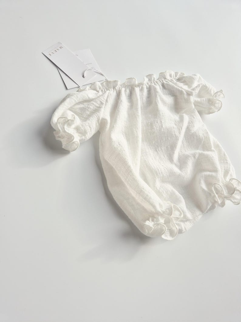 Angled studio shot of an ivory infant romper emphasizing the organic, highly textured crinkle cotton weave. This effortless, no-iron photography prop provides a luminous and tactile visual element for professional flat lay setups.