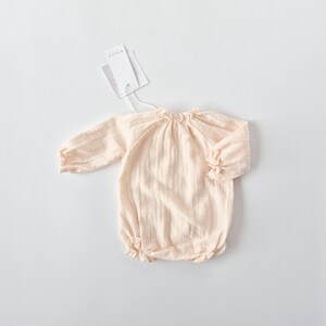 Minimalist flat lay of the Lylou warm vanilla long-sleeve romper. The pre-softened, crinkled fabric texture is clearly visible. A timeless newborn gift or coming home outfit piece for baby girls.