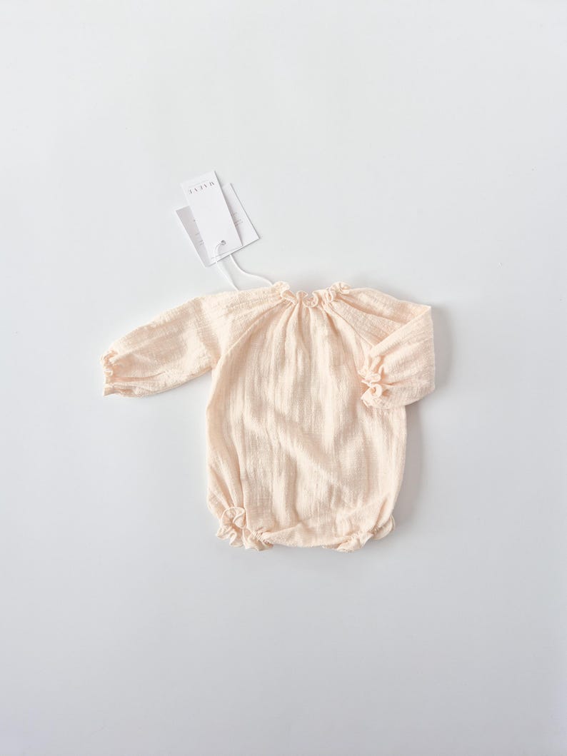 Minimalist flat lay of the Lylou warm vanilla long-sleeve romper. The pre-softened, crinkled fabric texture is clearly visible. A timeless newborn gift or coming home outfit piece for baby girls.