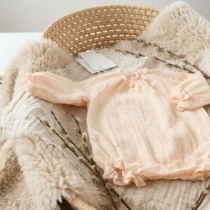 Close-up of the Lylou vanilla newborn romper resting in a basket. The premium 100% breathable crinkled cotton reveals 3D depth and buttery softness. Detailed shot of the smocked baby clothes texture.