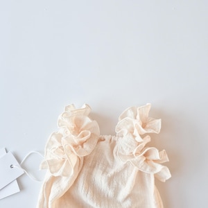 Detailed top-down view of an oversized frill collar on a baby girl romper. Creamy off-white textured cotton designed to drape beautifully over shoulders. Ideal baptism gift girl offering timeless elegance and a nostalgic glow.