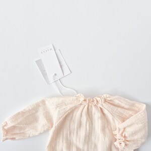 Studio lighting captures the upper bodice of the Lylou newborn romper with styling tags. The smocked neckline and warm cream tones make these luxury smocked baby clothes an ideal newborn hospital gift.