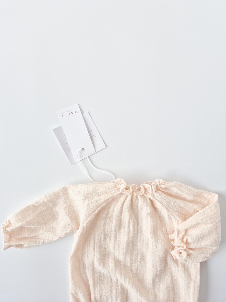 Studio lighting captures the upper bodice of the Lylou newborn romper with styling tags. The smocked neckline and warm cream tones make these luxury smocked baby clothes an ideal newborn hospital gift.