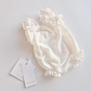 Slightly bunched ivory newborn outfit laid flat, emphasizing the soft, breathable Oeko-Tex cotton. The high-volume ruffles and relaxed fit showcase a highly functional, elegant hello world outfit ready for hospital photos.