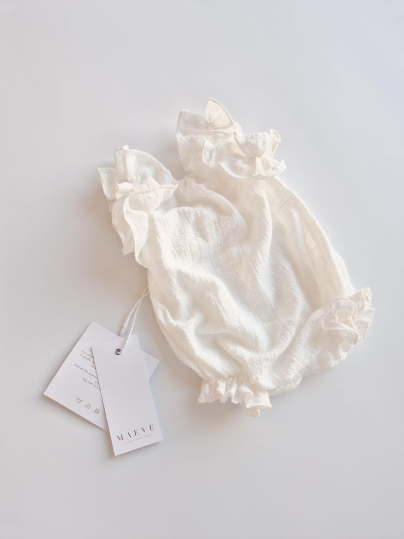 Slightly bunched ivory newborn outfit laid flat, emphasizing the soft, breathable Oeko-Tex cotton. The high-volume ruffles and relaxed fit showcase a highly functional, elegant hello world outfit ready for hospital photos.
