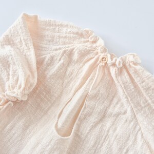 Close-up of warm vanilla Lylou baby romper showing tactile crinkled cotton texture and delicate back button closure. Perfect newborn photography props emphasizing breathable fabric and minimalist aesthetic.