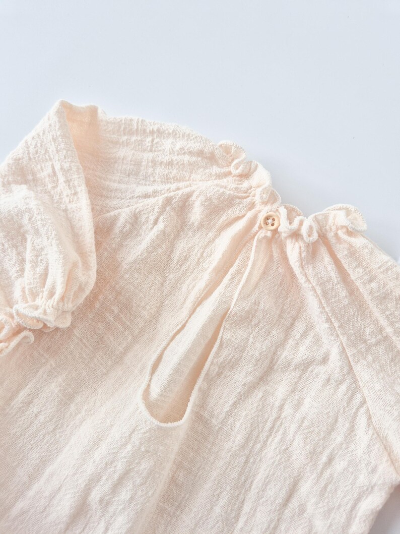 Close-up of warm vanilla Lylou baby romper showing tactile crinkled cotton texture and delicate back button closure. Perfect newborn photography props emphasizing breathable fabric and minimalist aesthetic.