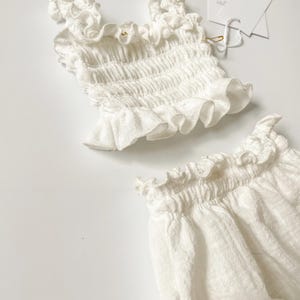 Close-up macro studio shot highlighting the elastic waistband and ruffled edges of a white crinkle cotton two-piece set. The crisp, tactile fabric behavior is captured under soft light, ideal for boutique and natural baby shower gifts.