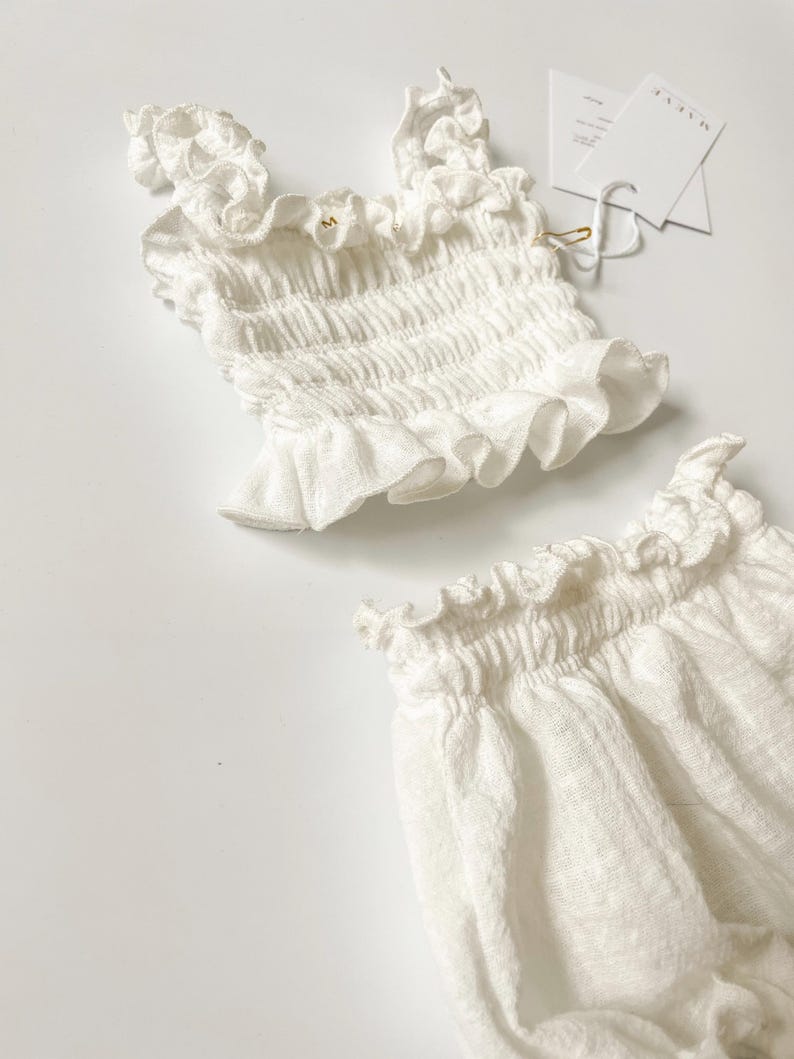 Close-up macro studio shot highlighting the elastic waistband and ruffled edges of a white crinkle cotton two-piece set. The crisp, tactile fabric behavior is captured under soft light, ideal for boutique and natural baby shower gifts.