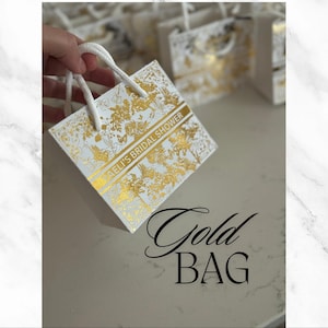 May include: White gift bag with a gold floral pattern and the text "[Name]'s Bridal Shower".