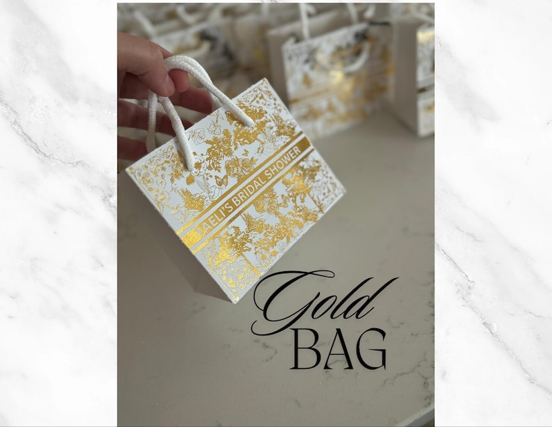 May include: White gift bag with a gold floral pattern and the text "[Name]'s Bridal Shower".