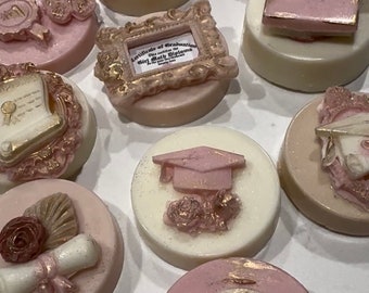 Peut inclure: Assortiment de neuf biscuits ronds enrobés de chocolat décorés sur le thème de la remise des diplômes. Les biscuits présentent des accents roses et dorés, avec des motifs comprenant un bonnet de diplômé, un diplôme, un livre et un certificat.