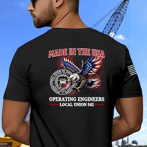 May include: Black t-shirt with "MADE IN THE USA" text and an eagle graphic with red, white, and blue wings. Below the eagle is a circular emblem with "OPERATING ENGINEERS LOCAL UNION 542" text.