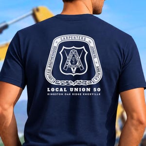 Può includere: Una t-shirt blu navy con una grafica bianca sul retro. Il design include l'emblema della United Brotherhood of Carpenters and Joiners of America, con il testo "Labor Vincit", "Local Union 50" e "Kingston Oak Ridge Knoxville" in bianco.